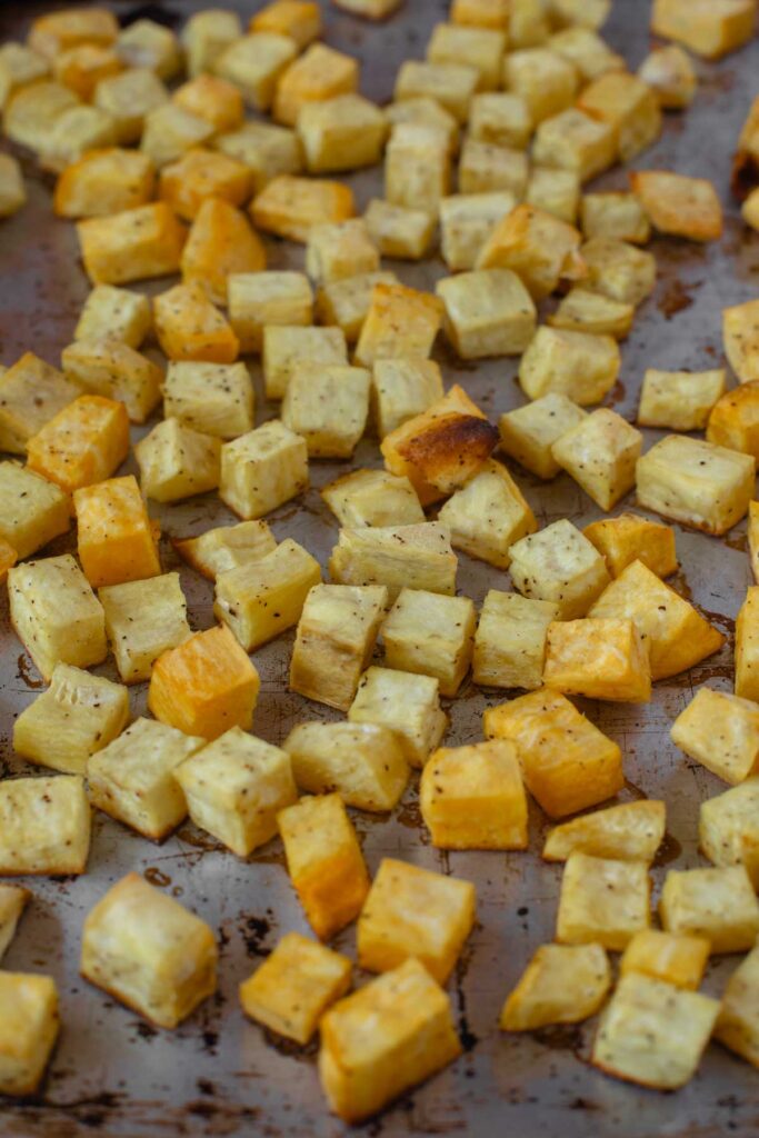 Small cubes of roasted yellow root vegetables, perfect for Sweet Potato and Black Bean Tacos, are spread on a baking sheet, showing a mix of golden brown and lightly toasted pieces.