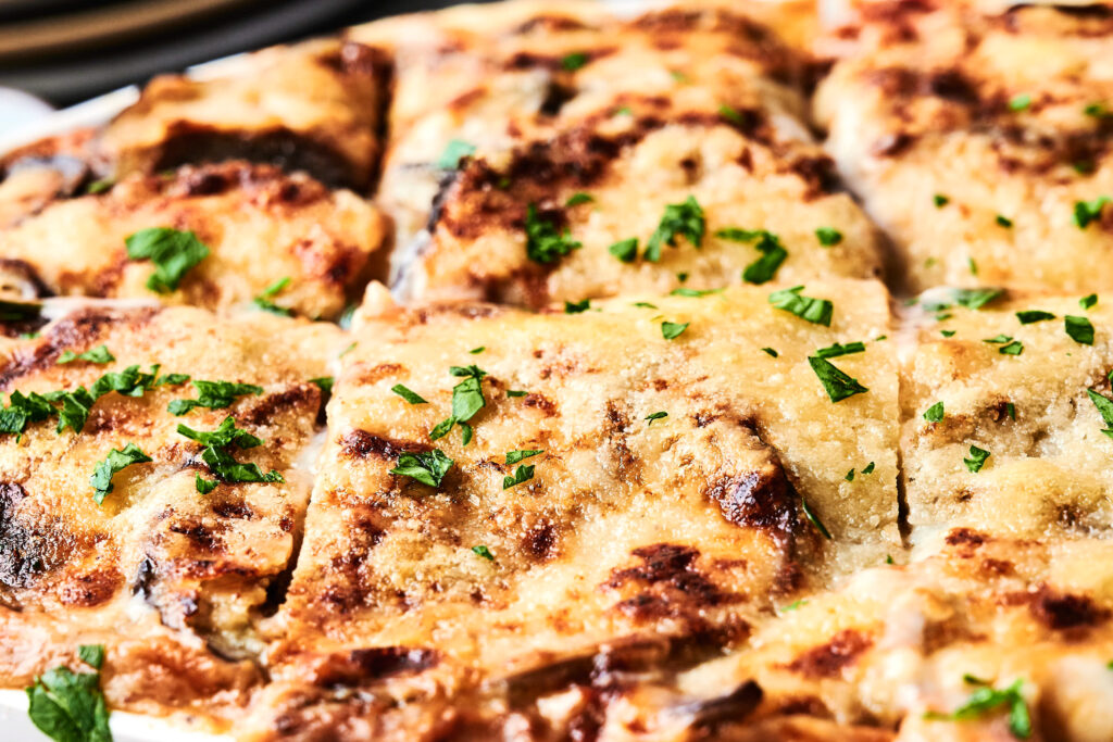 Close-up of Air Fryer Beef Moussaka, a baked dish topped with melted cheese and sprinkled with chopped parsley, cut into square pieces.