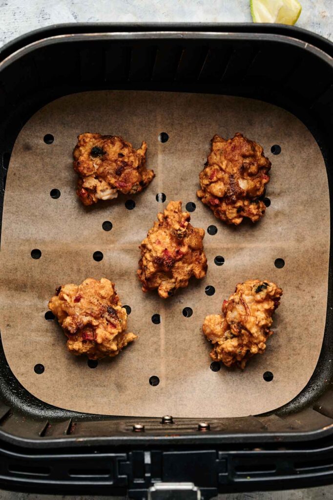 Five pieces of Air Fryer Conch Fritters sit on a sheet of perforated parchment paper inside an air fryer basket.
