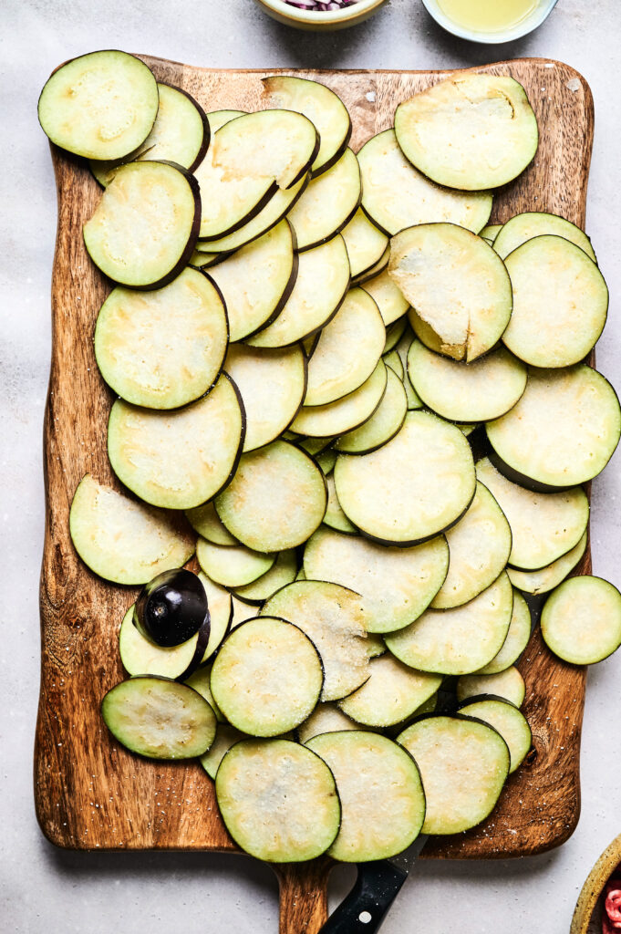 Sliced raw eggplant arranged on a wooden cutting board with a knife and a partially sliced eggplant nearby, perfect for preparing Air Fryer Beef Moussaka.