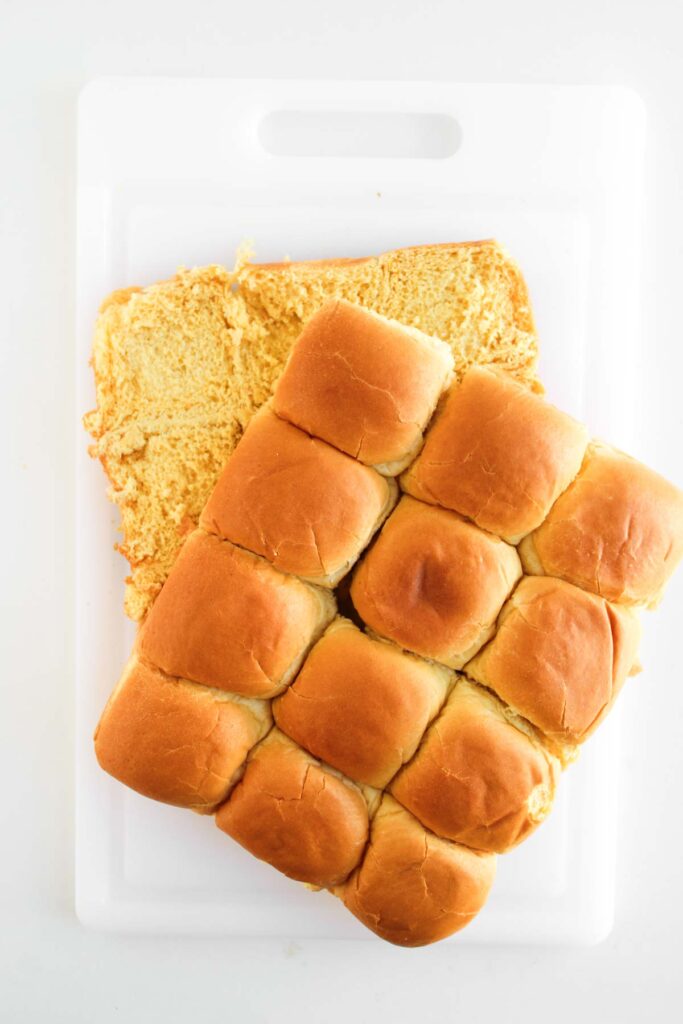 A sheet of twelve Cowboy Sliders dinner rolls, partially sliced horizontally, sits on a white cutting board.