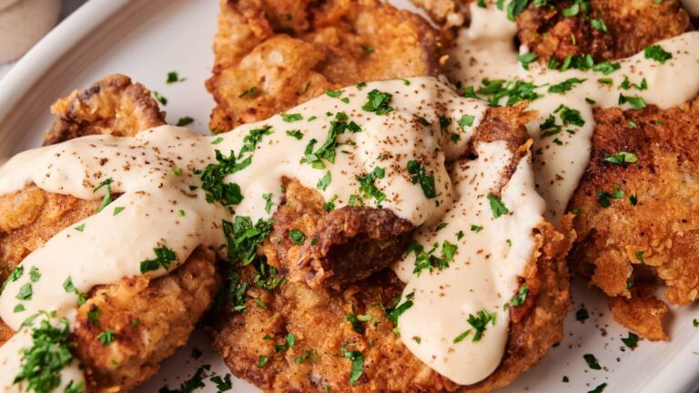 A plate of fried steak covered in creamy white gravy and garnished with chopped parsley.