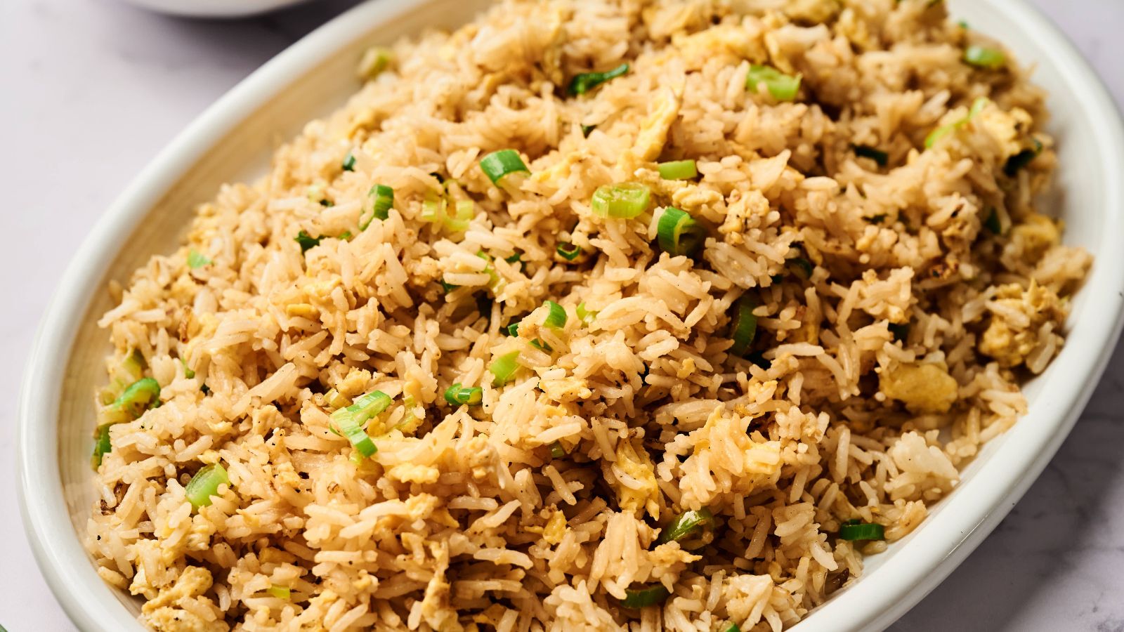 Oval dish filled with fried rice garnished with chopped green onions.