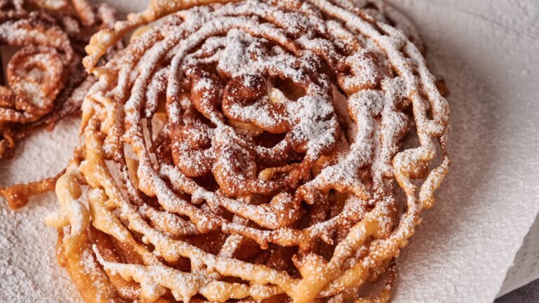 A close-up of a funnel cake topped with powdered sugar, resting on a paper towel.