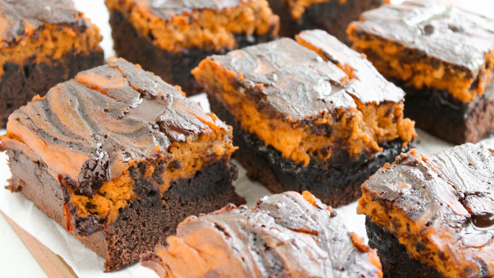 Close-up of several chocolate brownies with a swirl of orange filling on top, arranged on parchment paper.