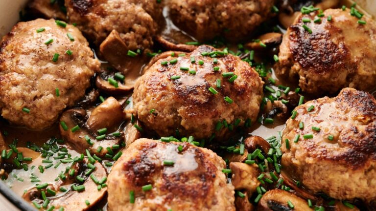 Six browned meat patties in a creamy mushroom sauce, garnished with chopped chives.