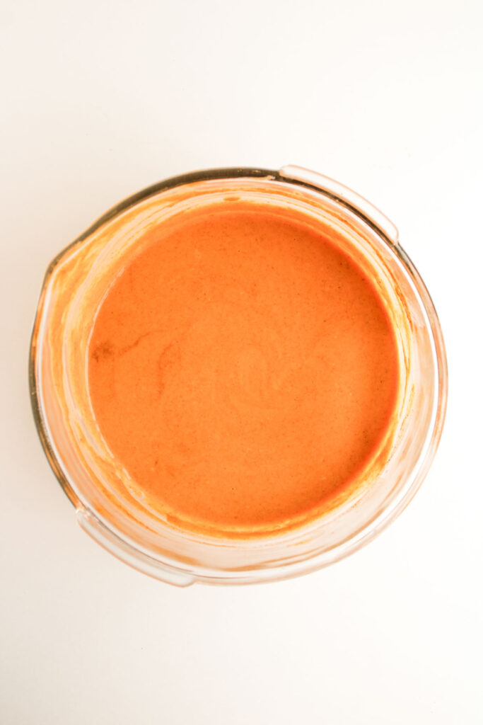 A glass bowl filled with a smooth, orange-colored mixture reminiscent of the filling for Pumpkin Pecan Pie Bars, viewed from above on a white background.