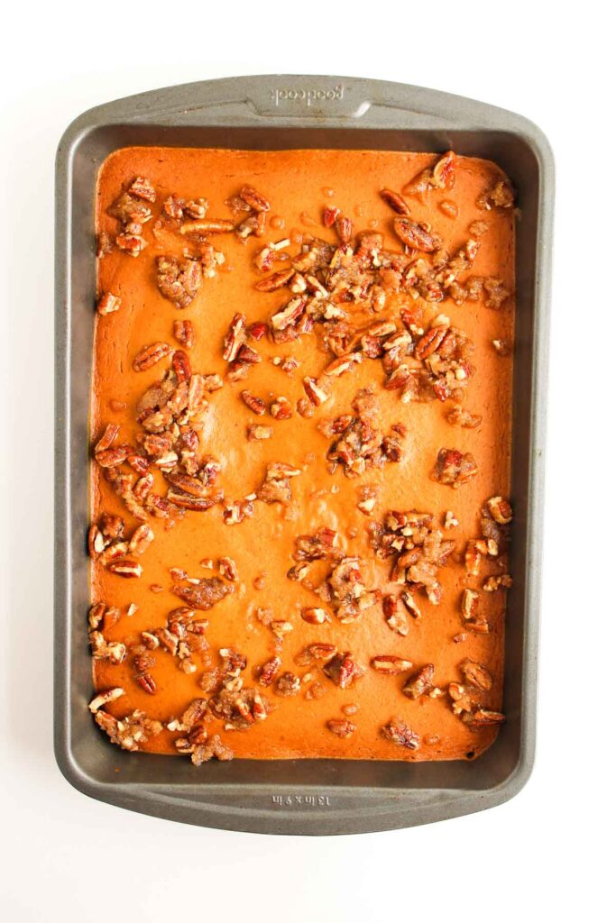 A rectangular baking pan containing Pumpkin Pecan Pie Bars, a baked dessert topped with chopped pecans, on a white background.