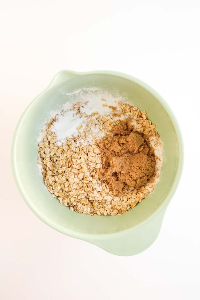 A green mixing bowl containing oats, brown sugar, and flour sits on a white surface, ready to be transformed into delicious Pumpkin Pecan Pie Bars.