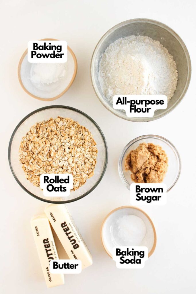 Six baking ingredients displayed in separate bowls and labeled: baking powder, all-purpose flour, rolled oats, brown sugar, butter sticks, and baking soda—perfect for making Pumpkin Pecan Pie Bars.