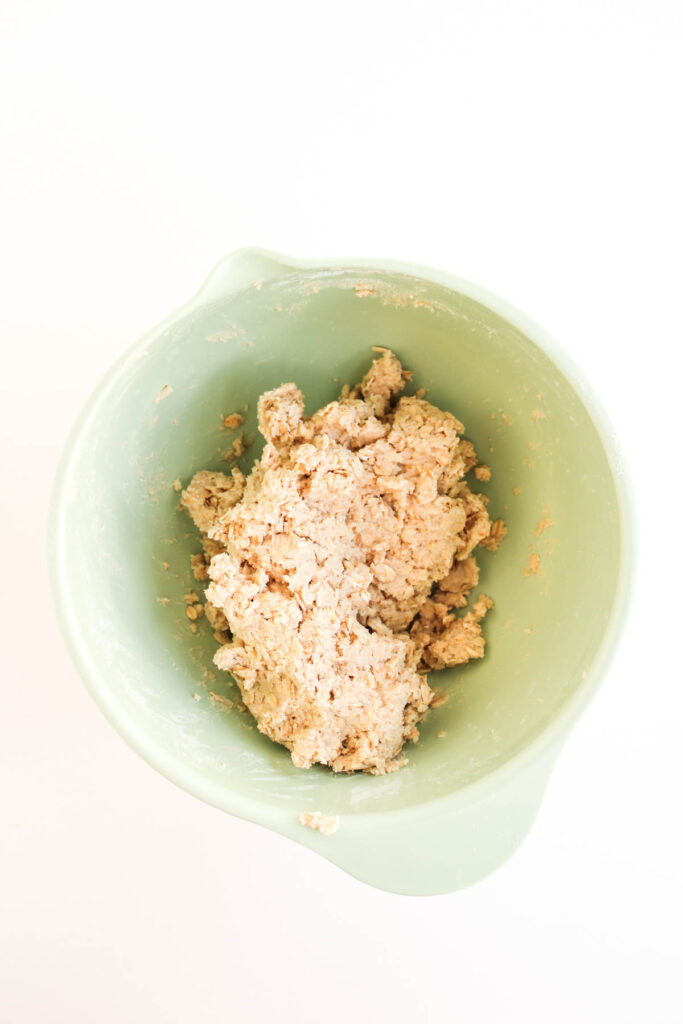 A green mixing bowl containing partially mixed dough for Pumpkin Pecan Pie Bars on a white background.