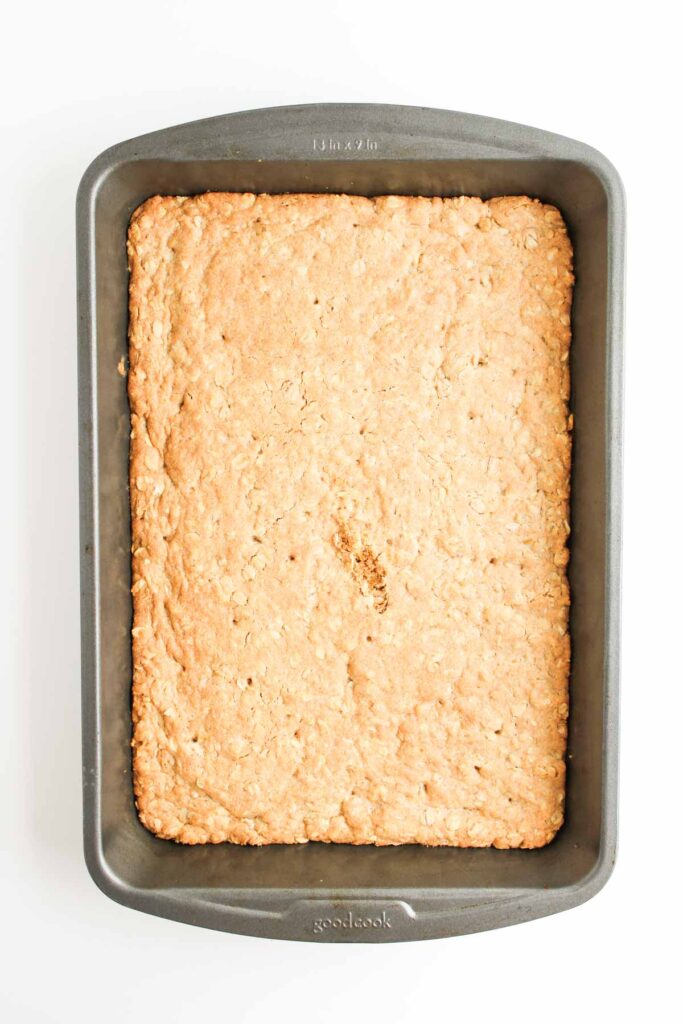 A rectangular pan of Pumpkin Pecan Pie Bars sits on a white surface, with a small crack visible in the center of the golden brown top.