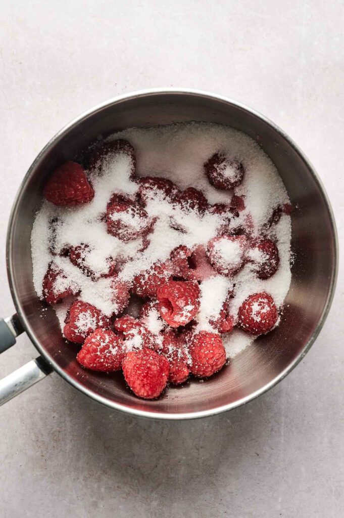 Fresh raspberries and granulated sugar in a metal saucepan, viewed from above, ready to be cooked or mixed&mdash;perfect for topping your Air Fryer Raspberry Cheesecake.