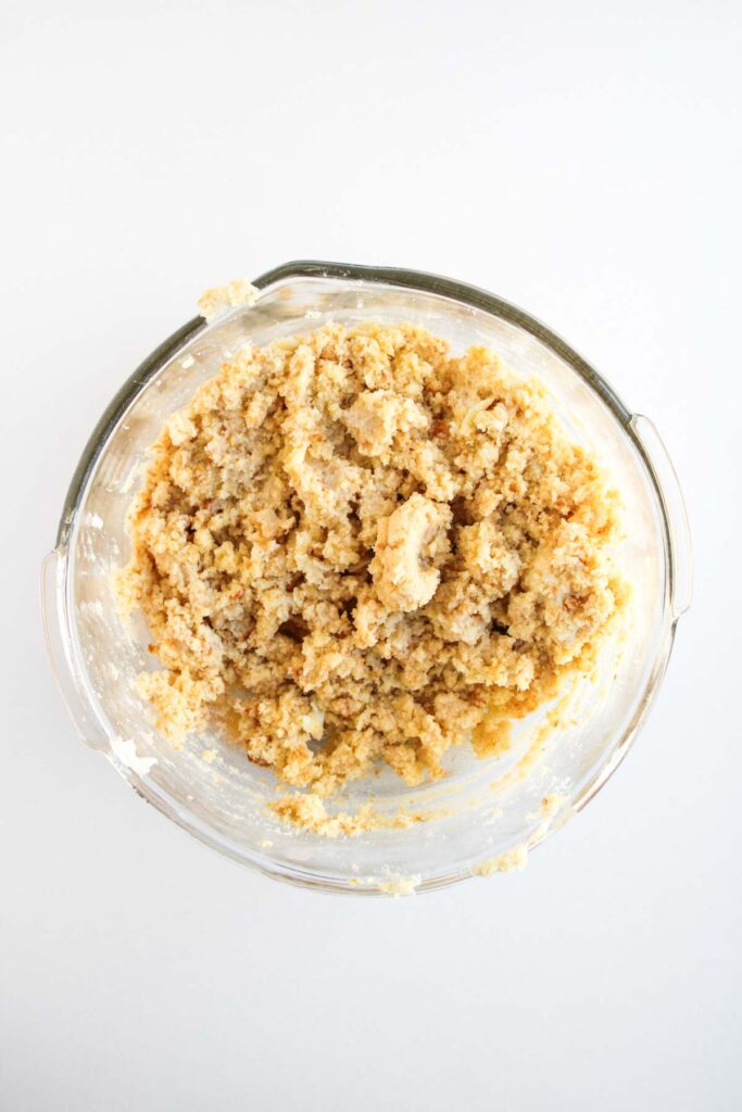 A glass mixing bowl containing coarse, crumbly cookie dough&mdash;perfect for shaping into whimsical Worms and Dirt Cake Pops&mdash;rests on a white surface.
