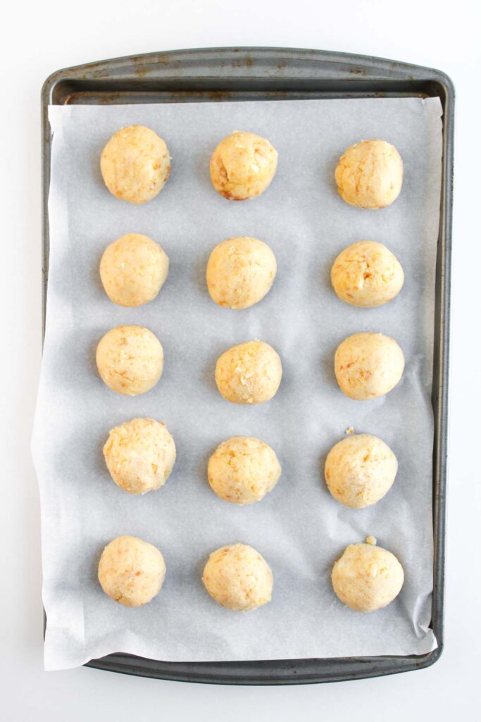 A baking sheet lined with parchment paper holds 15 evenly spaced, unbaked Worms and Dirt Cake Pops dough balls arranged in a grid pattern.