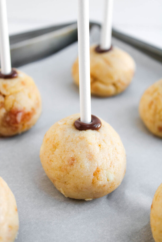 Worms and Dirt Cake Pops: Round cake pop balls on sticks, set on a parchment-lined baking sheet, with chocolate securing the sticks in place.
