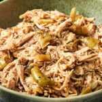 Shredded Crockpot Mississippi Chicken mixed with sliced green peppers and black pepper, served in a green ceramic bowl.