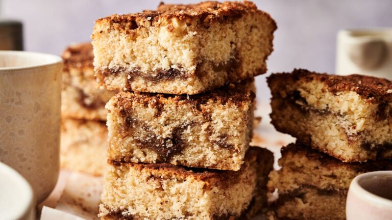 Three pieces of coffee cake stacked on top of each other, showing a cinnamon swirl in the middle, surrounded by mugs.