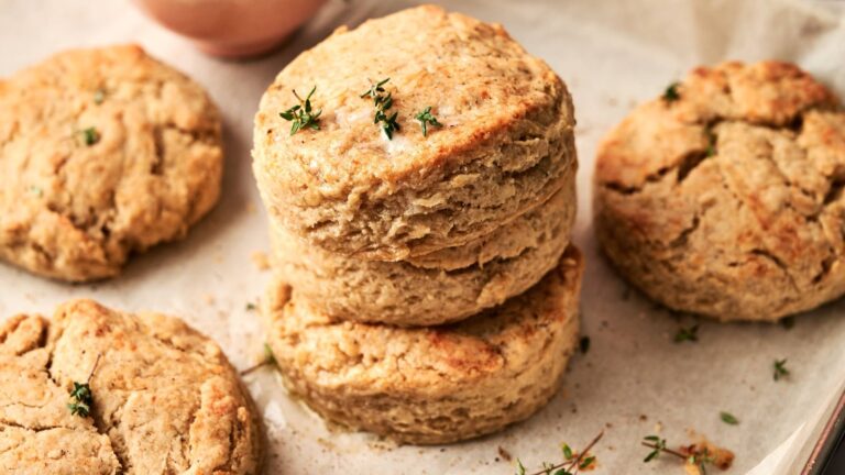 Four golden brown biscuits sit on parchment paper, with two stacked on top of each other and garnished with fresh thyme.