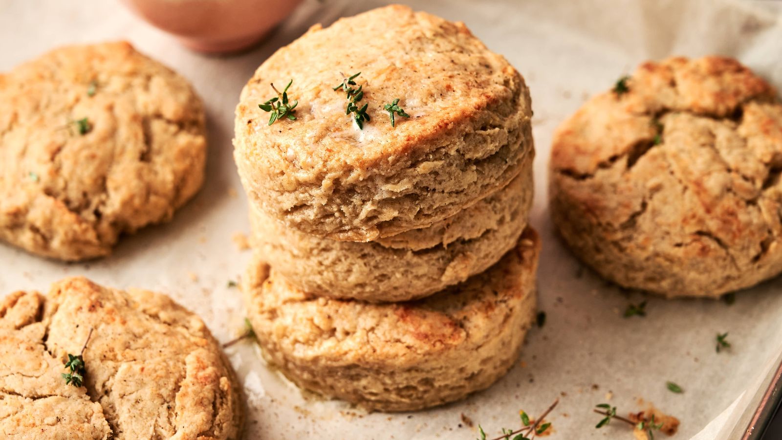 A close-up of several golden-brown biscuits stacked on parchment paper, garnished with a few sprigs of fresh herbs.
