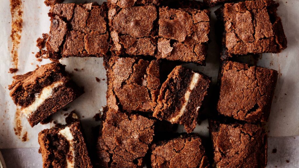 Top view of sliced chocolate brownies with a visible cream cheese layer, arranged on parchment paper.
