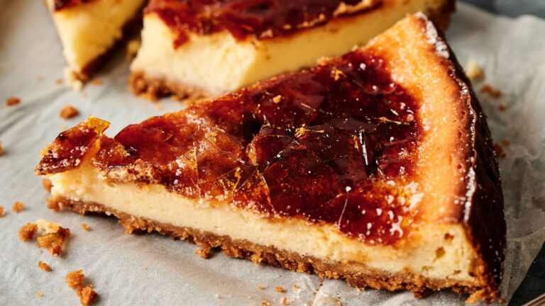 A slice of cheesecake with a caramelized sugar topping and a crumbly crust sits on parchment paper.