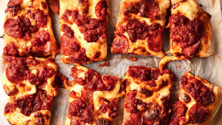 Eight rectangular slices of thick-crust pizza with melted cheese and chunky tomato sauce arranged on parchment paper.