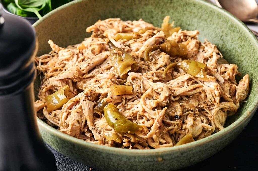 Shredded chicken with green peppers and seasoning, inspired by Crockpot Mississippi Chicken, served in a green bowl.