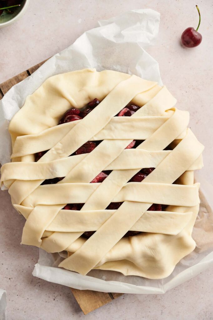 Unbaked cherry pie with a golden lattice crust on parchment paper, this classic Cherry Pie is ready for the oven.