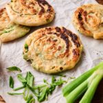 Three cooked Scallion Pancakes rest on parchment paper, served with a small bowl of dipping sauce and fresh sliced scallions on the side.