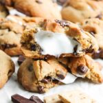 A stack of S’mores Stuffed Cookies with gooey marshmallow filling—some cookies are whole, while one is split open to reveal the irresistibly soft center.