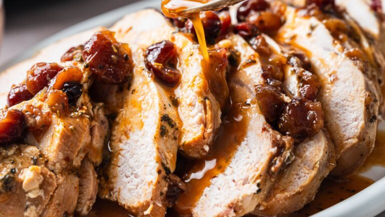 Sliced roasted turkey breast topped with a fruit-based sauce being drizzled over it on a plate.