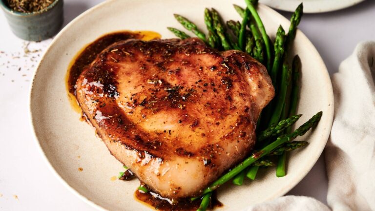 A grilled pork chop with brown sauce served on a plate with cooked asparagus spears.