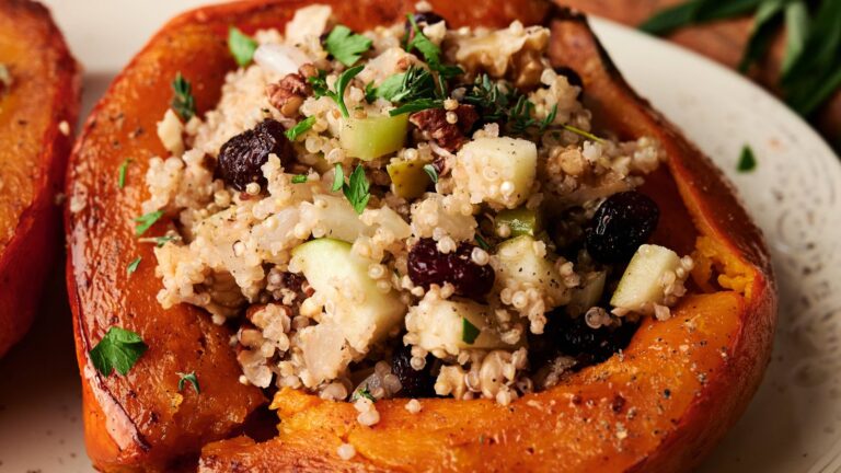A roasted squash half filled with a stuffing mixture of couscous, apples, raisins, herbs, and nuts, served on a white plate.