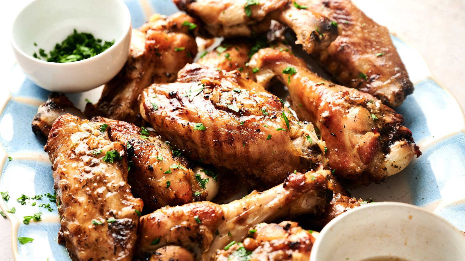 A plate of cooked chicken wings garnished with chopped herbs, accompanied by two small bowls of dipping sauces.