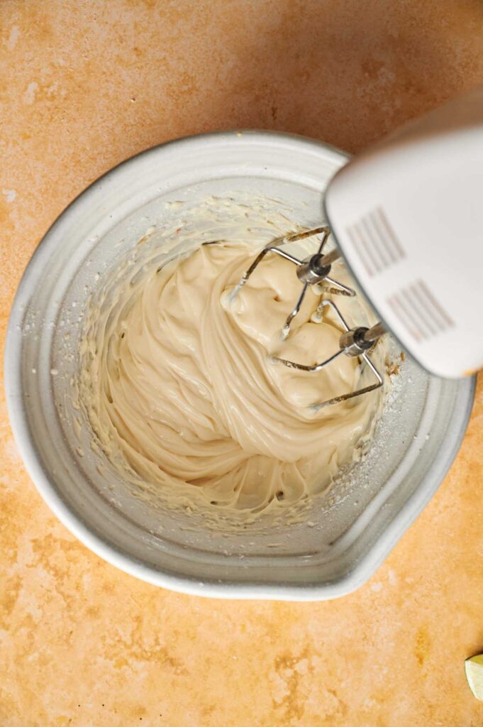 Electric hand mixer blending creamy batter for a Pumpkin Cake in a white mixing bowl on a light orange countertop.