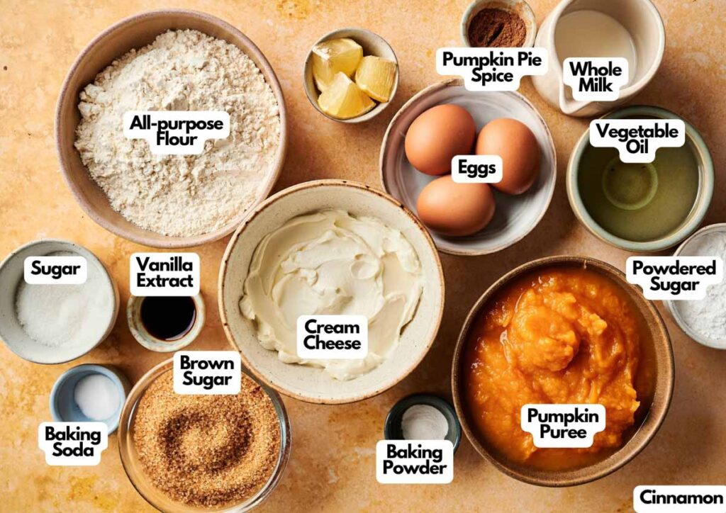 Top-down view of baking ingredients in bowls for Pumpkin Cake, including flour, sugars, cream cheese, pumpkin puree, eggs, spices, baking powder, baking soda, vanilla extract, vegetable oil, and milk.