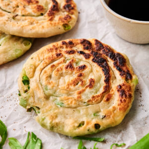 Two delicious Scallion Pancakes rest on parchment paper, garnished with sliced green onions and served next to a small bowl of dark dipping sauce.