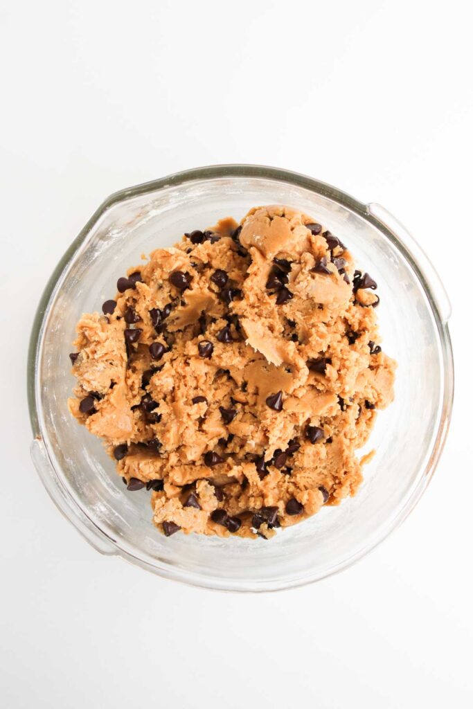 A glass bowl filled with S&rsquo;mores Stuffed Cookies chocolate chip cookie dough sits on a white background.
