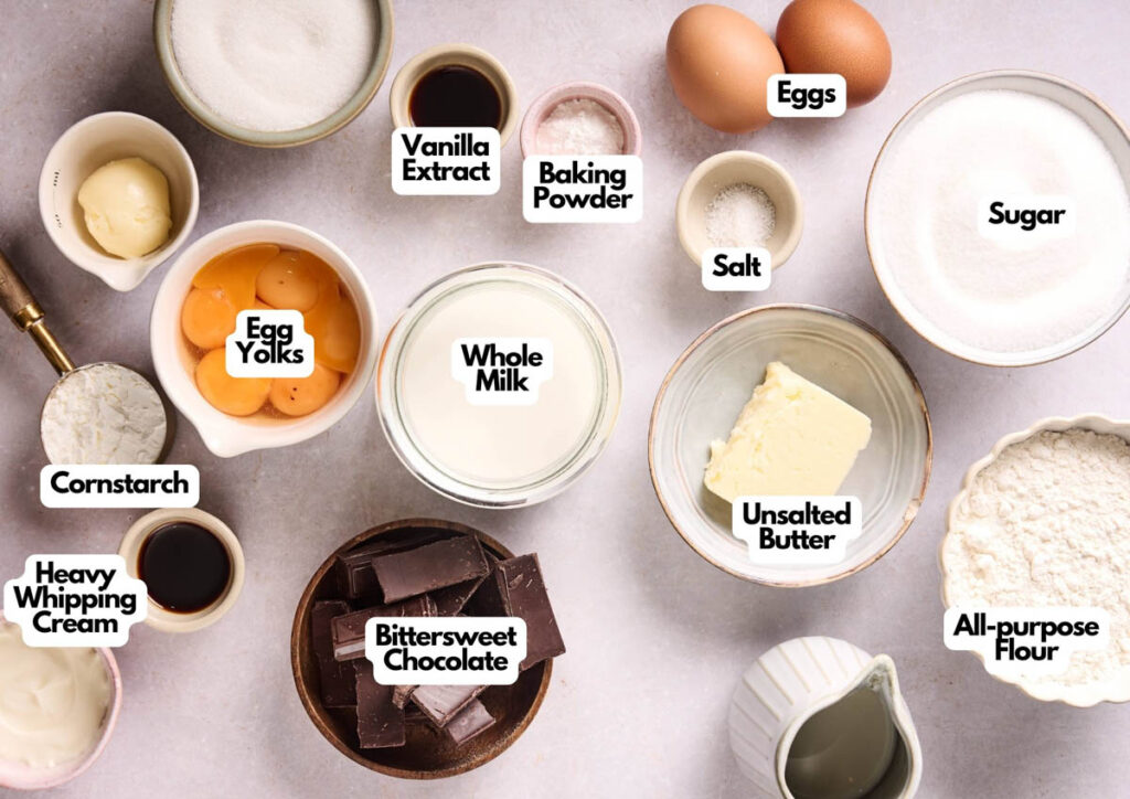 Various baking ingredients labeled in bowls and containers, including eggs, sugar, flour, butter, bittersweet chocolate, milk, egg yolks, and others—perfect for creating a classic Boston Cream Pie—are arranged on a light surface.