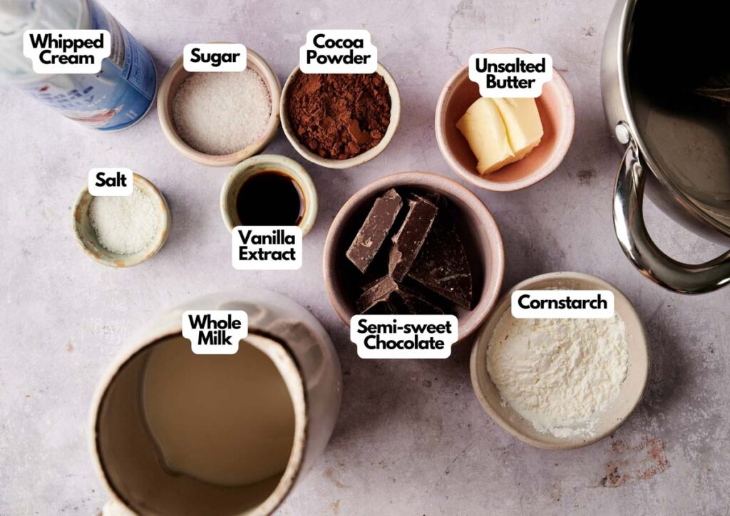 Various ingredients in labeled bowls for Chocolate Pudding, including whipped cream, sugar, cocoa powder, unsalted butter, salt, vanilla extract, semi-sweet chocolate, whole milk, and cornstarch.