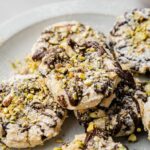 A plate of Cannoli Cookies topped with powdered sugar, chopped pistachios, and drizzled with chocolate.