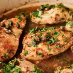 Close-up of Chicken Piccata featuring cooked chicken breasts in a brown sauce, garnished with chopped parsley and capers.