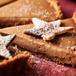 A close-up of a sliced Eggnog Pie with a crumbly crust, topped with a star-shaped cookie and dusted with powdered sugar.