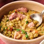A bowl of Ham and Split Pea Soup with chunks of ham, diced carrots, and parsley, with a spoon resting in the bowl.