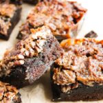 Close-up of Pecan Pie Brownies topped with a layer of chopped pecans and caramelized topping, arranged on a sheet of parchment paper.
