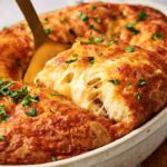 A close-up of a cheesy, golden-brown Sloppy Joe Casserole being served from a white dish, topped with chopped parsley.