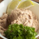 A white bowl filled with smoked mackerel pate, garnished with two lemon wedges and a sprig of parsley.