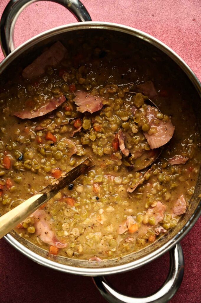 A pot of Ham and Split Pea Soup with visible chunks of ham, diced carrots, and a wooden spoon resting inside.
