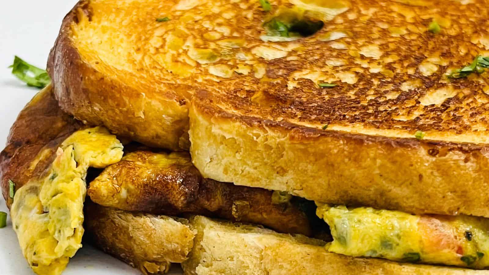 A close-up of a toasted sandwich filled with scrambled eggs and garnished with green herbs.